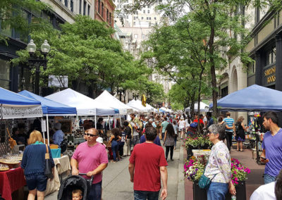 People walking by Westminster Street filled with shops and flowers in downtown Providence, RI.